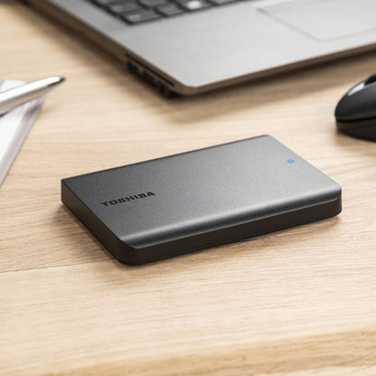 Toshiba Canvio Basics ekstern harddisk 4 TB sorteret ved siden af laptop, mus og papirer på træskrivebord.