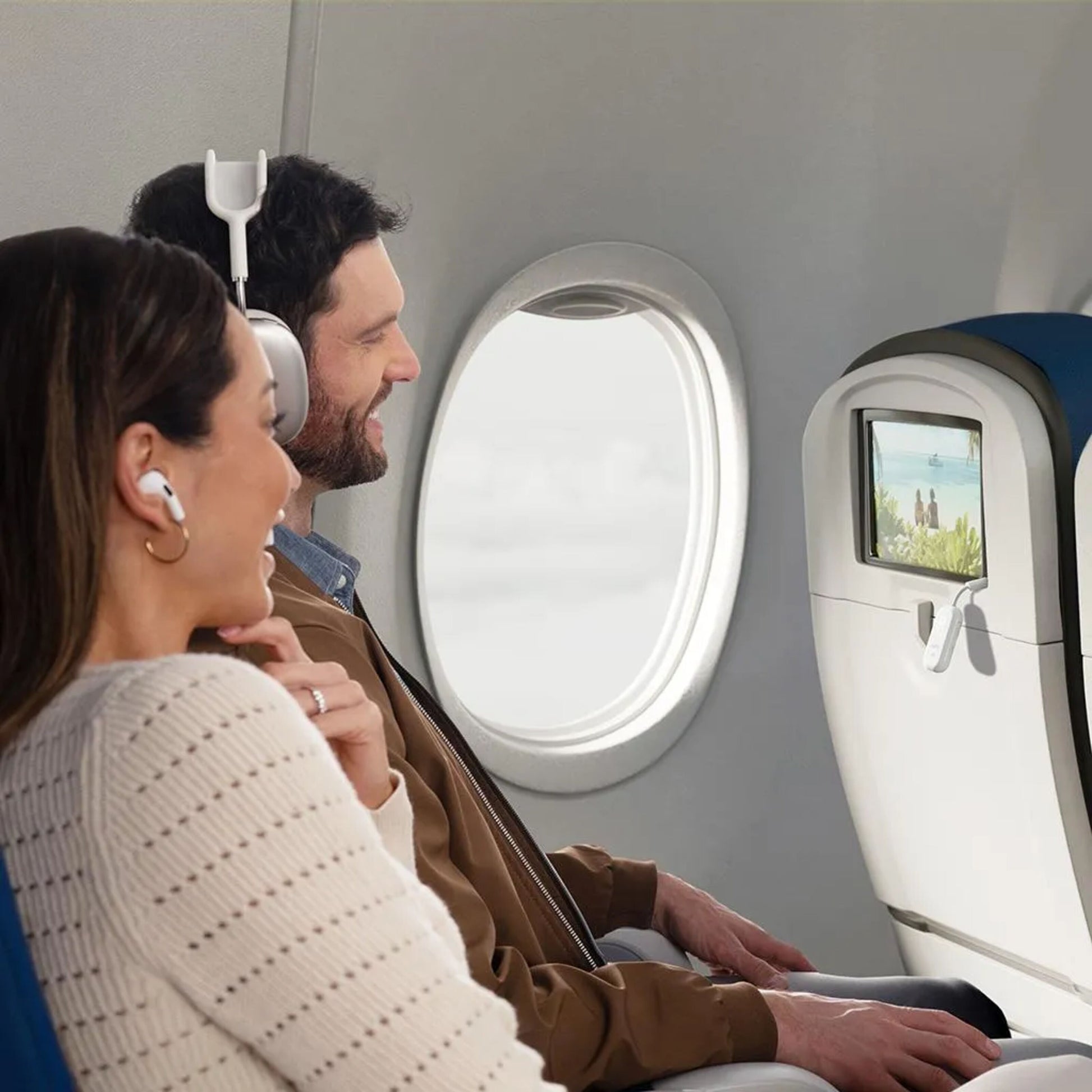 AirPods og sorte over-ear hovedtelefoner tilsluttet AirFly Pro 2 Bluetooth-sender synlig i flykabine ved vinduesplads.