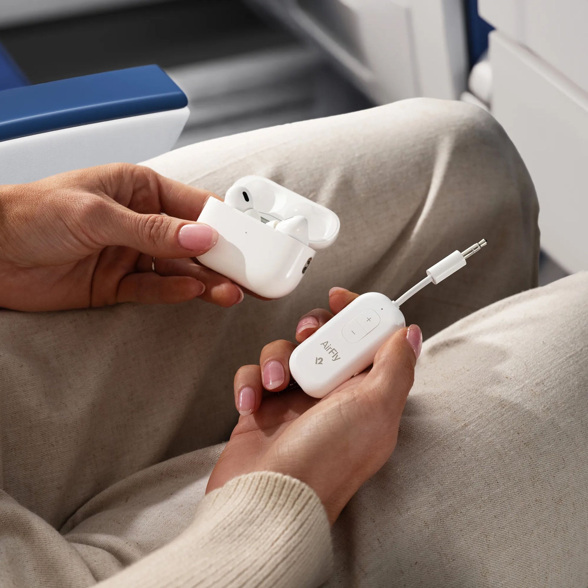 Twelve South AirFly Pro 2 Bluetooth-sender og -modtager samt trådløse ørepropper i opladningsetui på beige sæde.