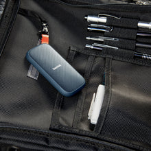 Sandisk bærbar SSD-harddisk 1TB med blå og orange detaljer i sort netlomme på taske, synlig USB-C port.