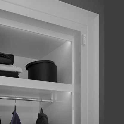 Philips Hue Sikker kontakt sensor Hvid 1-pak monteret i hvidt skab med tøj og sort opbevaringsboks, integreret lys.