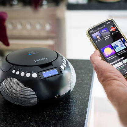 Lenco SCD-331 Sort bærbar CD-afspiller på køkkenbord ved siden af smartphone med musikapp i brug.