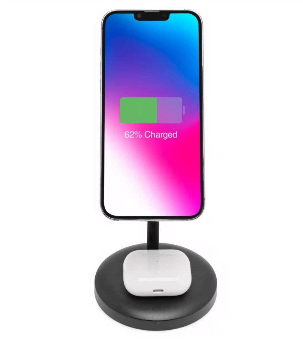 IPhone oplades trådløst med MagSafe på sort 2-i-1 opladningsstation, smartphone lodret, hvide øretelefoner ved basen.