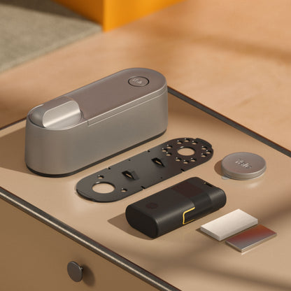 Yale Linus Smart Lock L2 sølv med genopladeligt batteri, monteringsplade, rund dækskive og selvklæbende strips.
