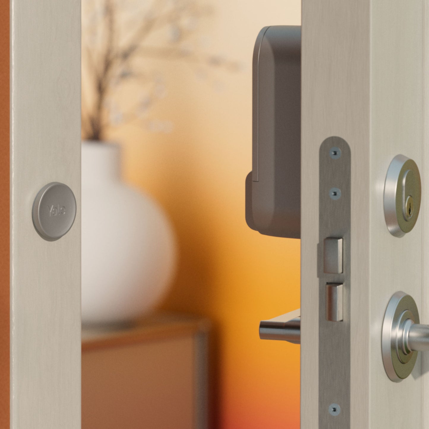 Yale Linus Smart Lock L2 Sølv på dør, synligt genopladeligt batteri, sløret hvid vase i baggrund.