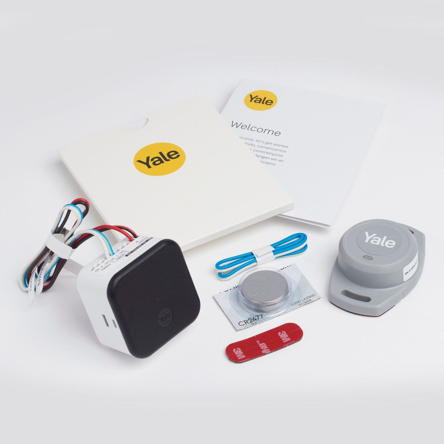 Yale Smart garageportåbner, sort/hvid enhed, stik, klæbestrimmel, blå USB-kabel, batteri, grå sensor, manualer.