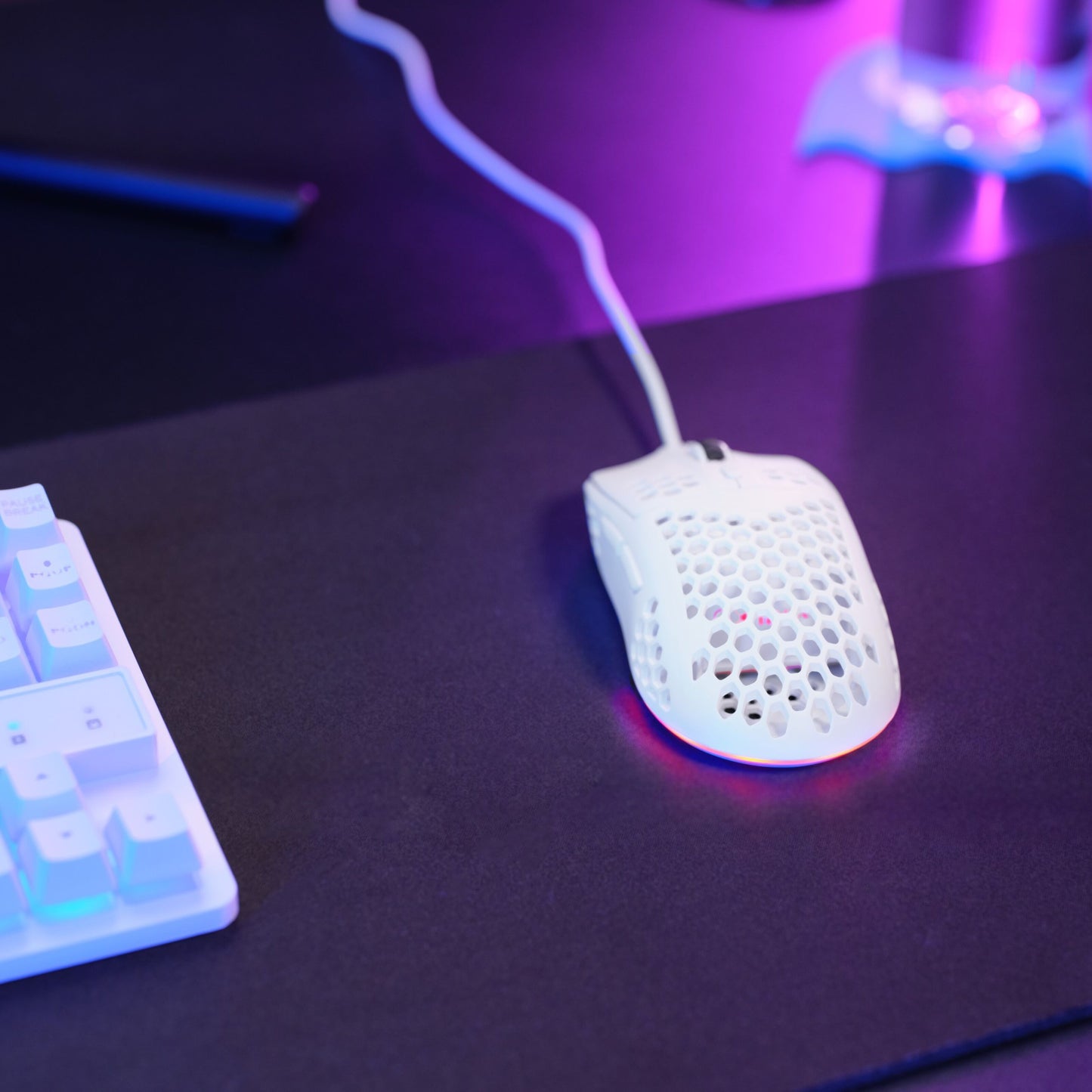 Trust GXT928 Helox letvægts gaming mus hvid honeycomb design justerbar DPI på sort musemåtte ved hvidt tastatur med lilla/blå lys.