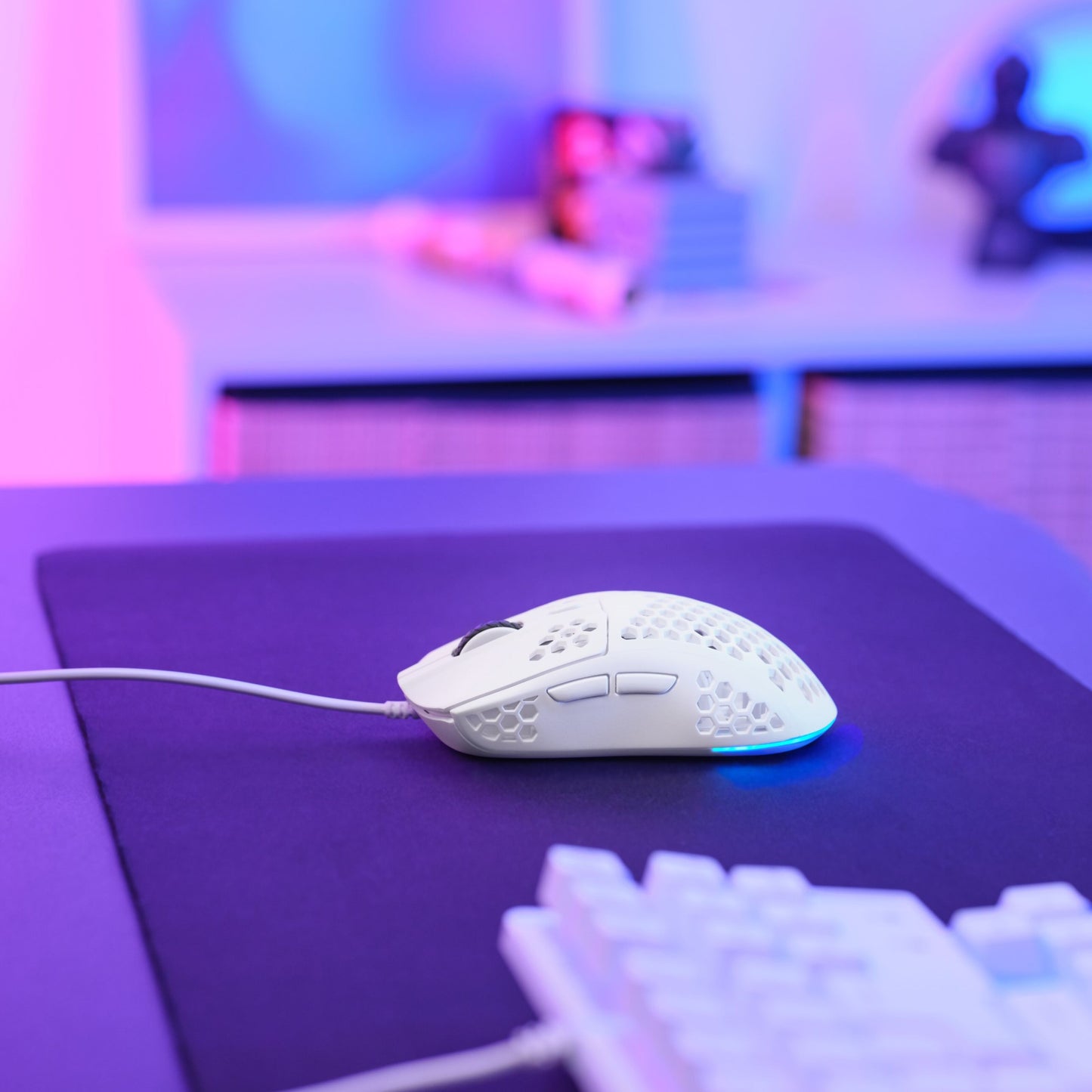 Trust Helox GXT928 letvægts gaming mus med honeycomb-mønster på stor mørk musemåtte ved siden af hvidt tastatur.
