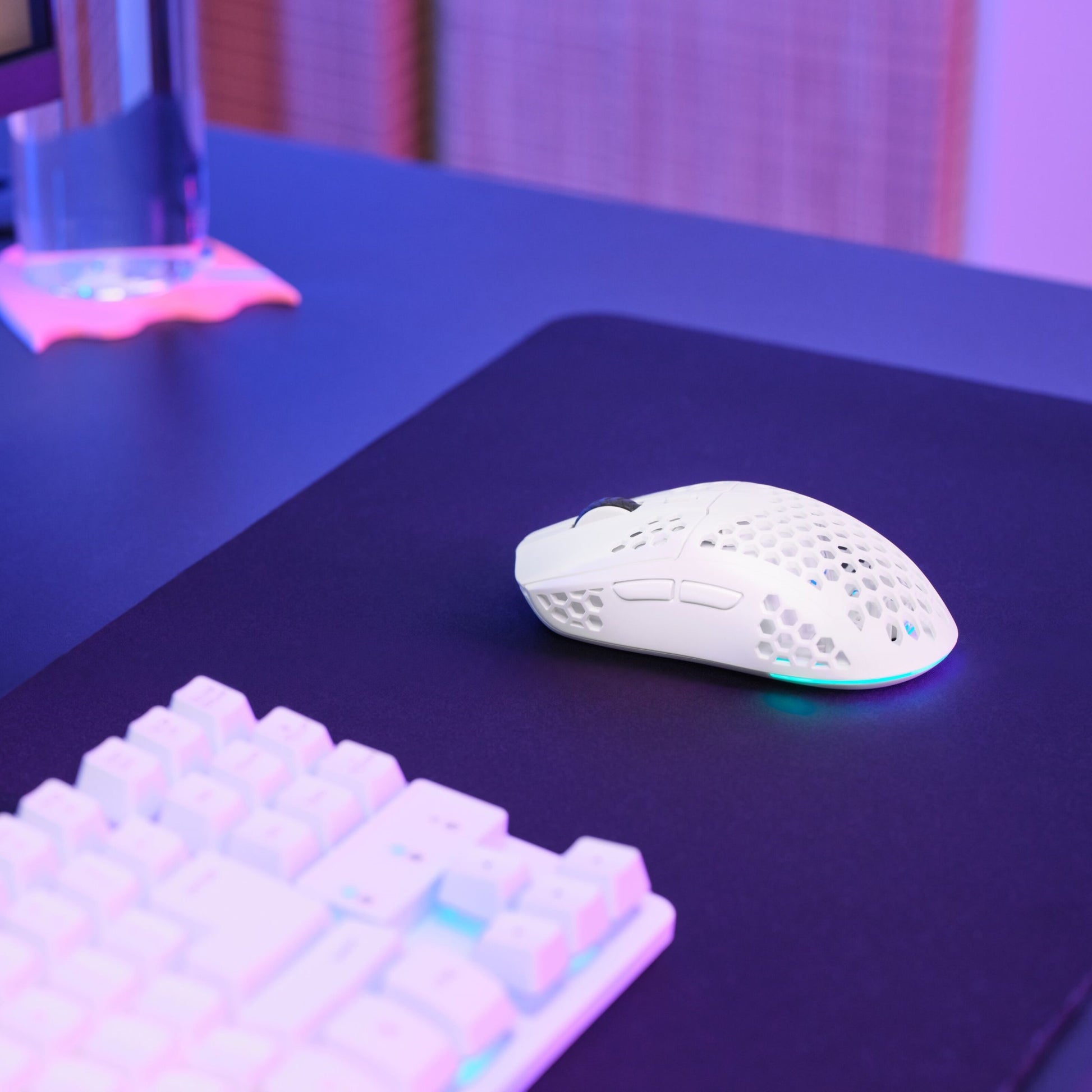 Trust Helox GXT929 trådløs gaming mus i hvid på stor sort musemåtte ved siden af hvidt tastatur, lilla/blåt lys.