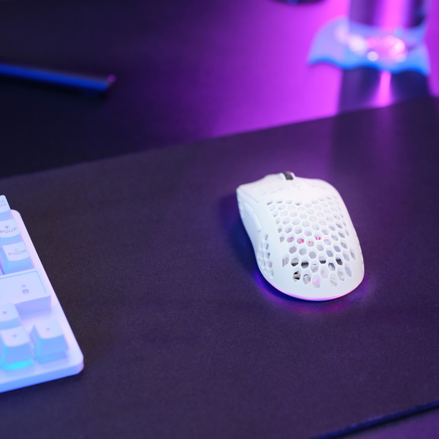 Trust Helox GXT929 trådløs hvid gamingmus med honeycomb-design på sort musemåtte ved siden af hvidt tastatur med pink/blå lys.