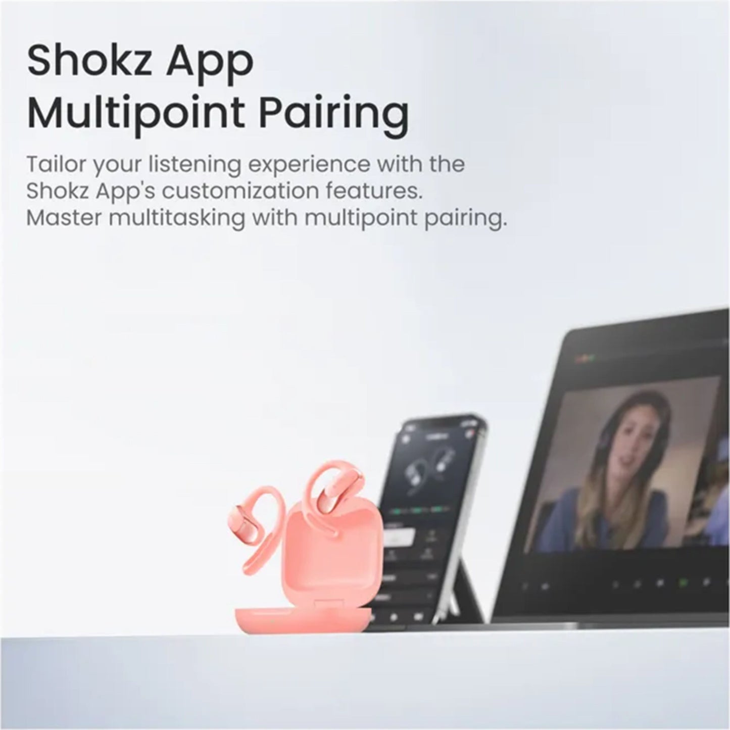 Shokz OpenFit Air trådløse hovedtelefoner lyserød i åbent opladningsetui ved aktiv smartphone og laptop, Shokz App vises.