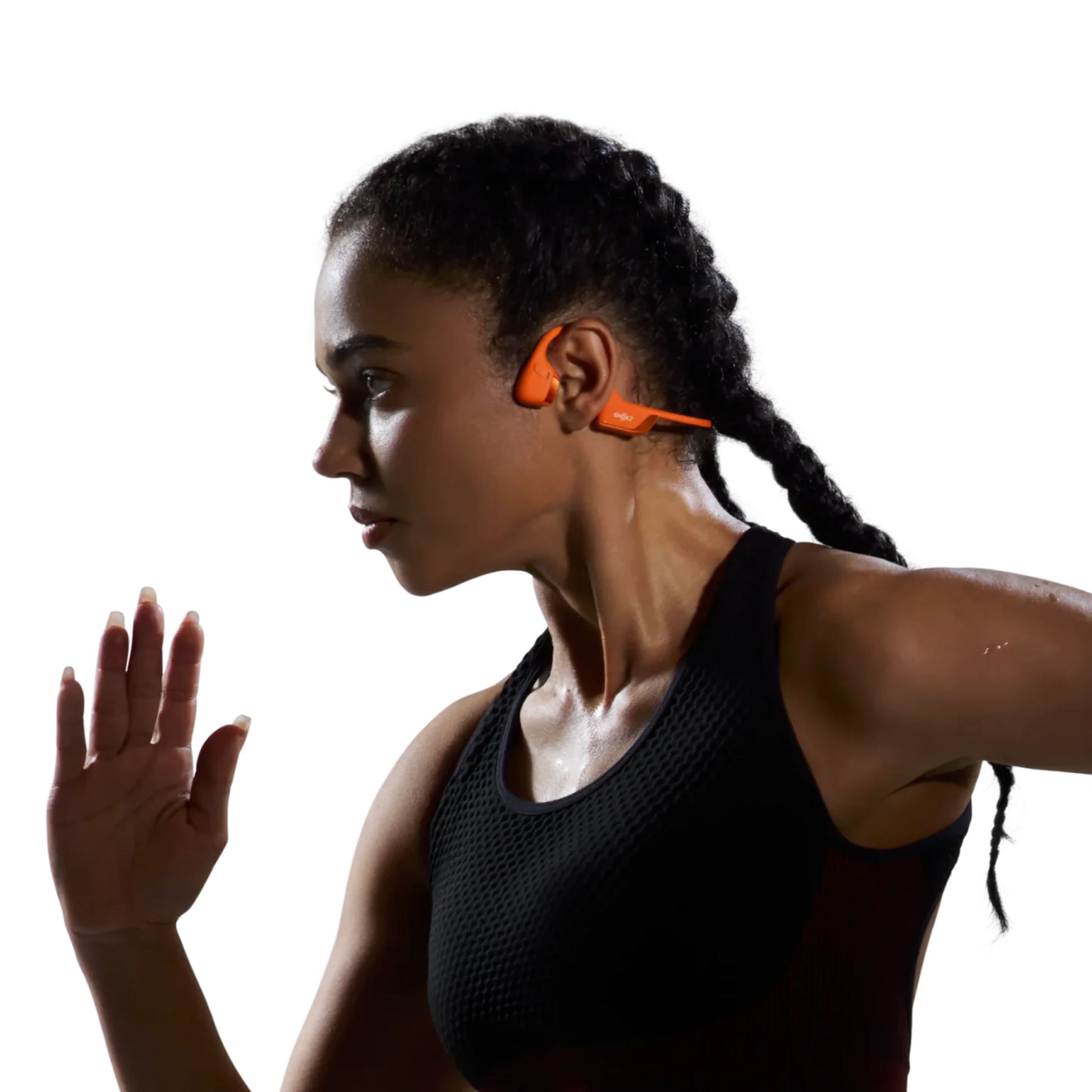 Kvinde med fletninger iført sorte sportstop og orange Shokz OpenRun Pro 2 Mini trådløse hovedtelefoner.