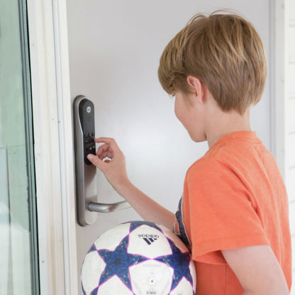 Yale Dørmand Klassisk Hjem elektronisk lås sølv, kodepanel, barn i orange trøje foran døren, fodbold i hånden.