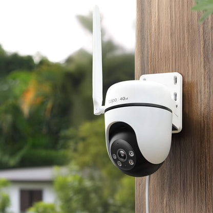 TP-Link Tapo C501GW udendørs 4G LTE kamera med antenne monteret på trævæg, grøn have sløret i baggrunden.