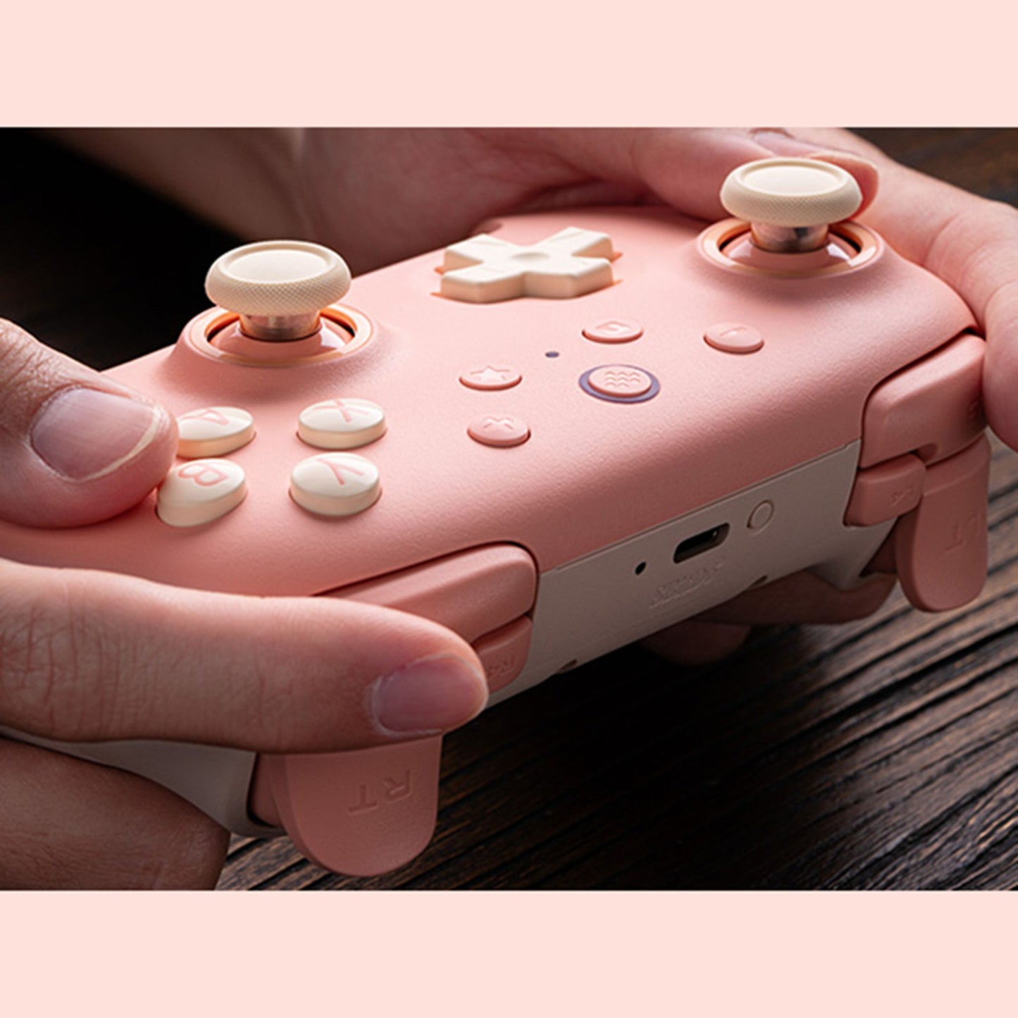 8Bitdo Ultimate 2C trådløs håndkontrol Hall Effect fersken pink/hvid med cremefarvede knapper, holdes i hænder.