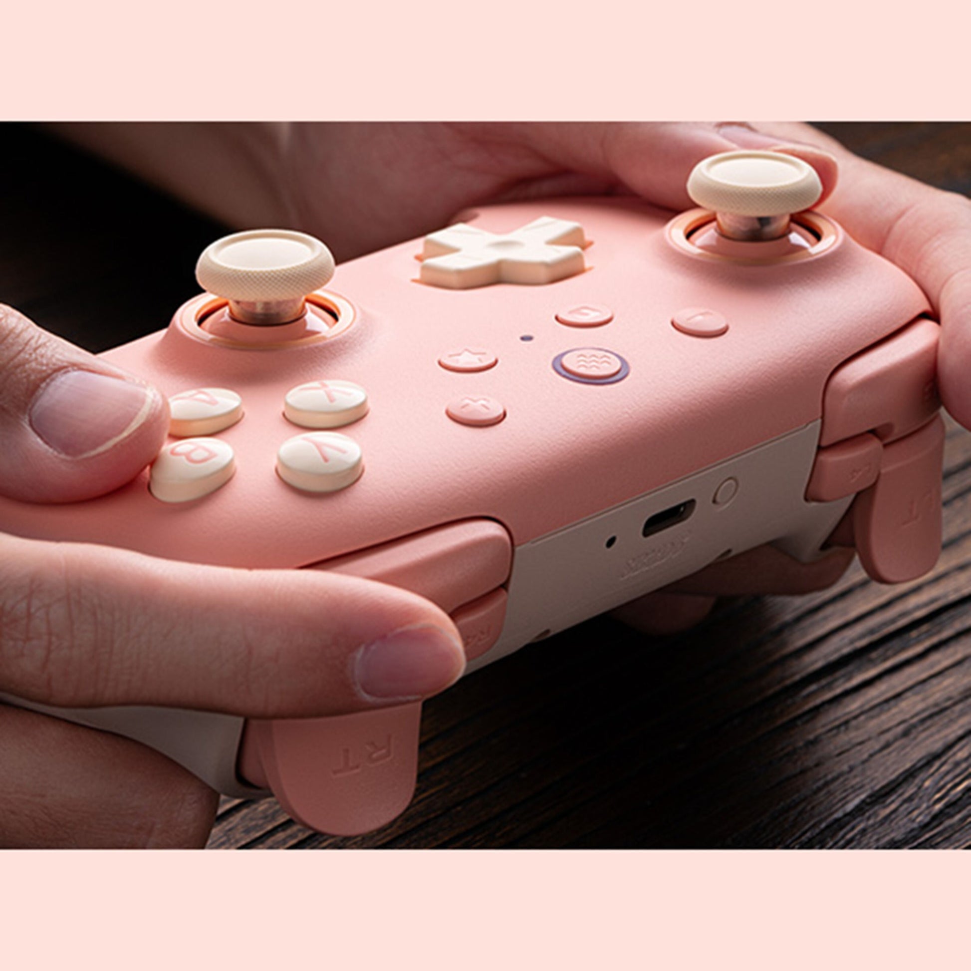8Bitdo Ultimate 2C trådløs håndkontrol Hall Effect fersken pink/hvid med cremefarvede knapper, holdes i hænder.