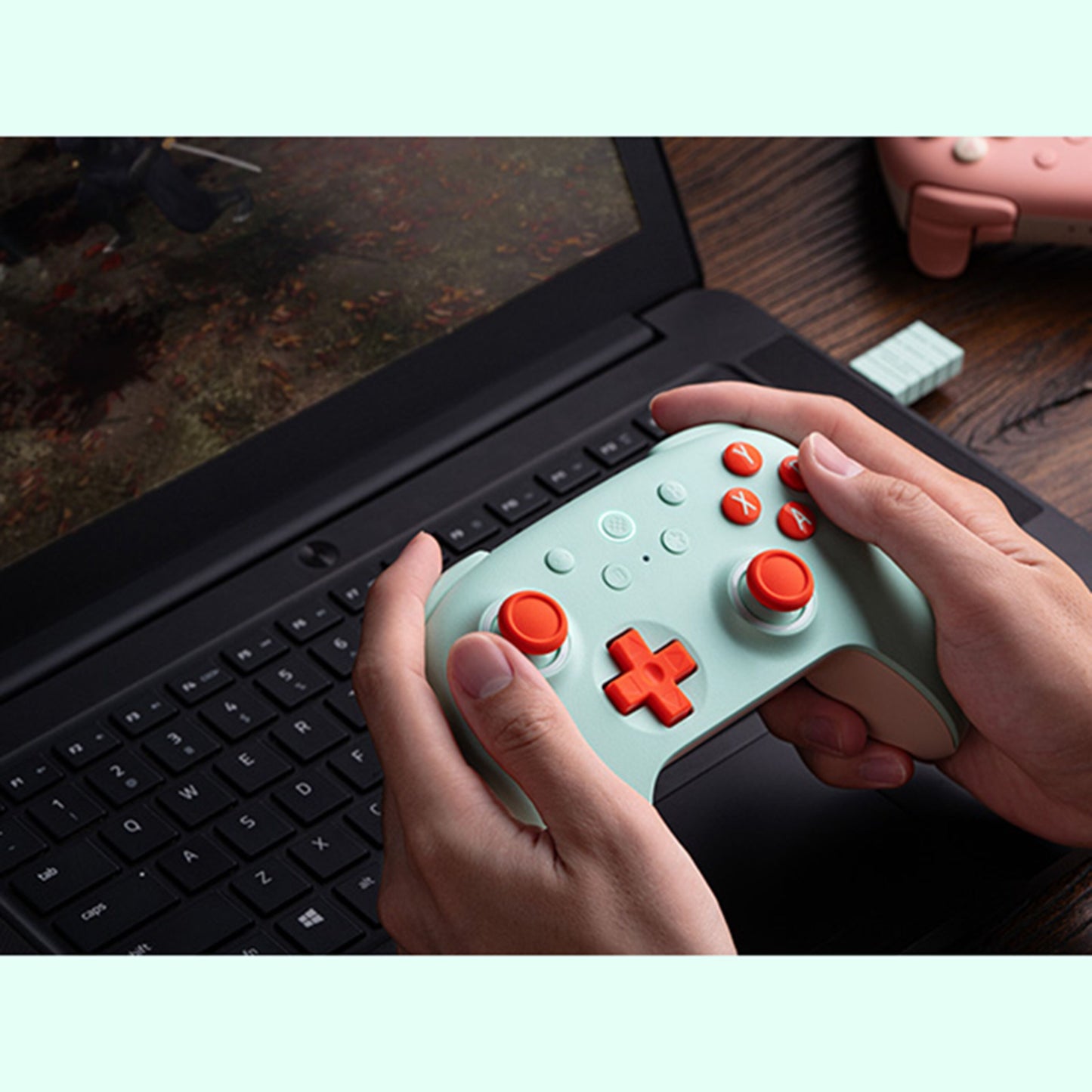 8Bitdo Ultimate 2C mint trådløs håndkontrol med Hall Effect vises i brug foran sort laptop, ekstra controller på træbord.