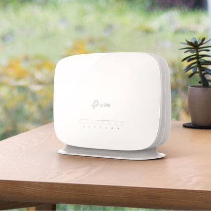 TP-Link Archer MR515 4G+ router med modem AC1200 sort står på bord ved vindue, lille potteplante ved siden af.