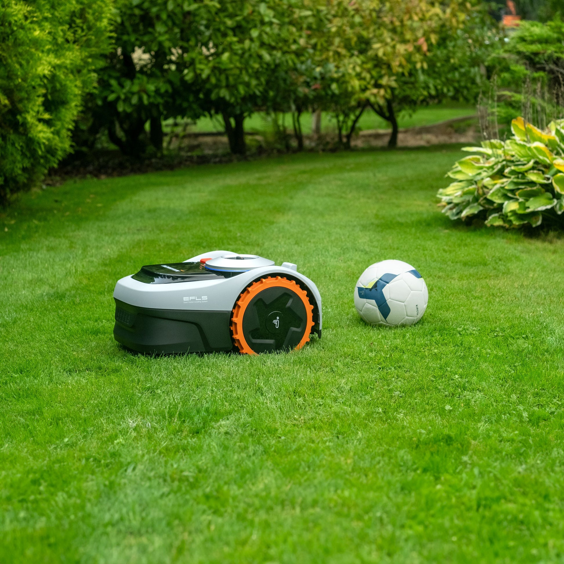 Segway Navimow i105e robotplæneklipper til 500 m² ved hvid og blå fodbold mellem grønne buske og planter.