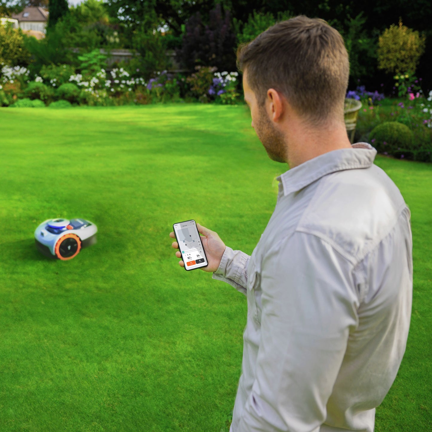 Segway Navimow i105e robotplæneklipper til 500 m² på græsplæne, mand med smartphone, træer og blomster i baggrunden.