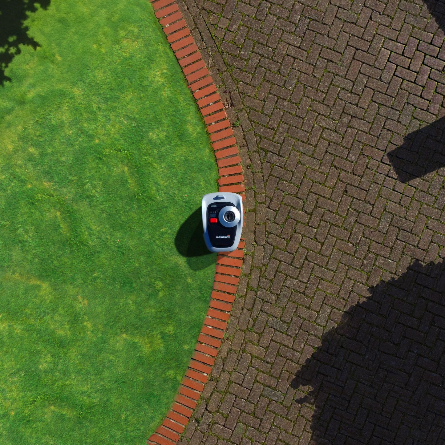 Segway Navimow i105e robotplæneklipper 500 m² ved grøn græsplæne og buet murstenskant mod fliseareal.