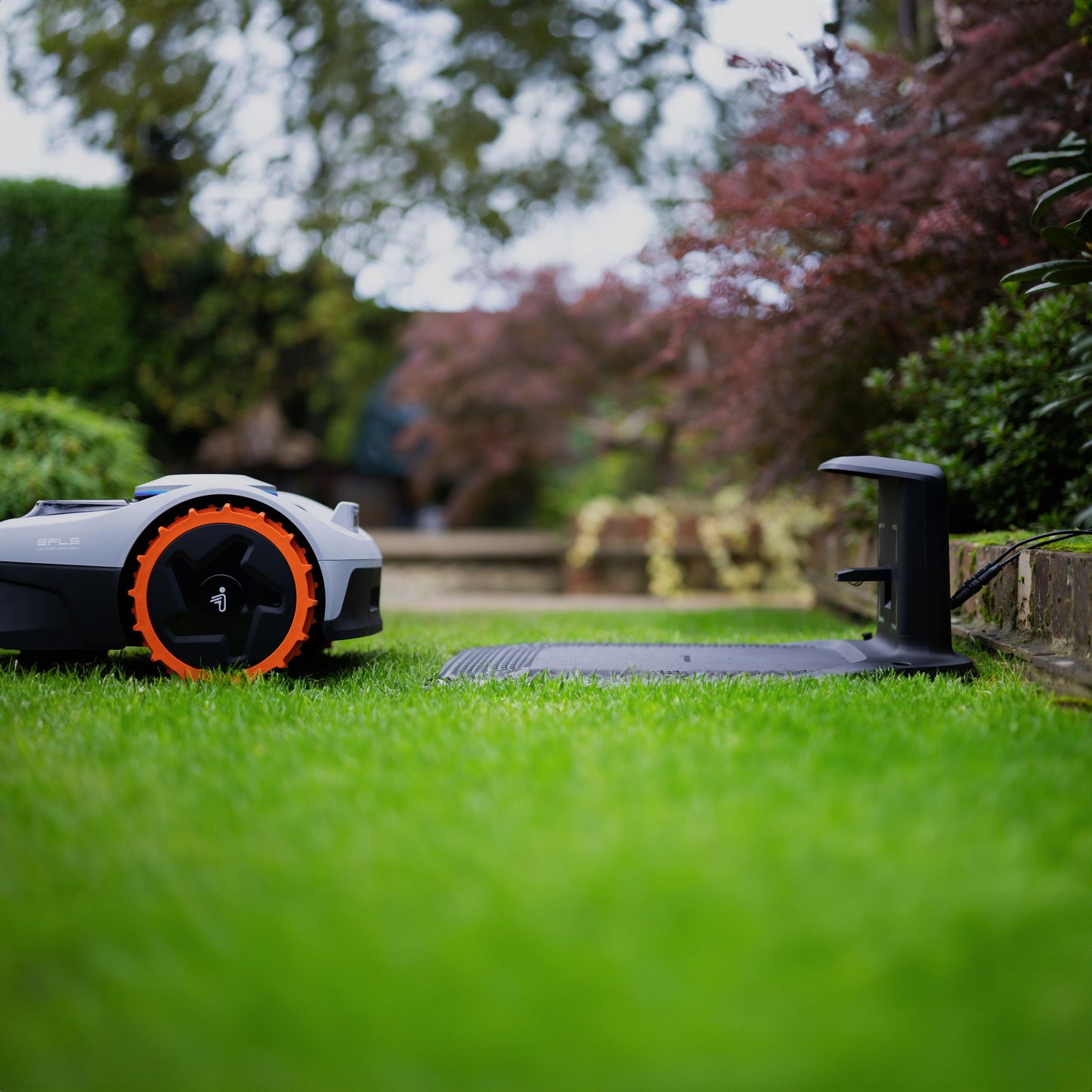 Segway Navimow i105e robotplæneklipper til 500 m² med orange hjul på vej mod sort ladestation på grøn plæne.
