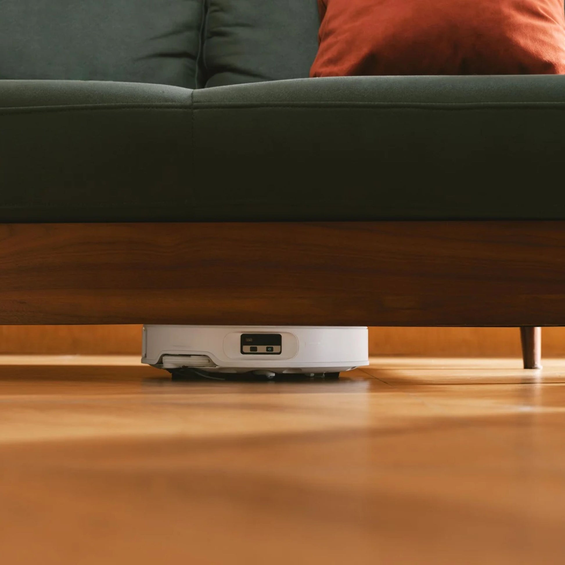 Roborock Qrevo Edge 2 Pro robotstøvsuger med moppe på trægulv under mørkegrøn sofa med træben og rød pude.