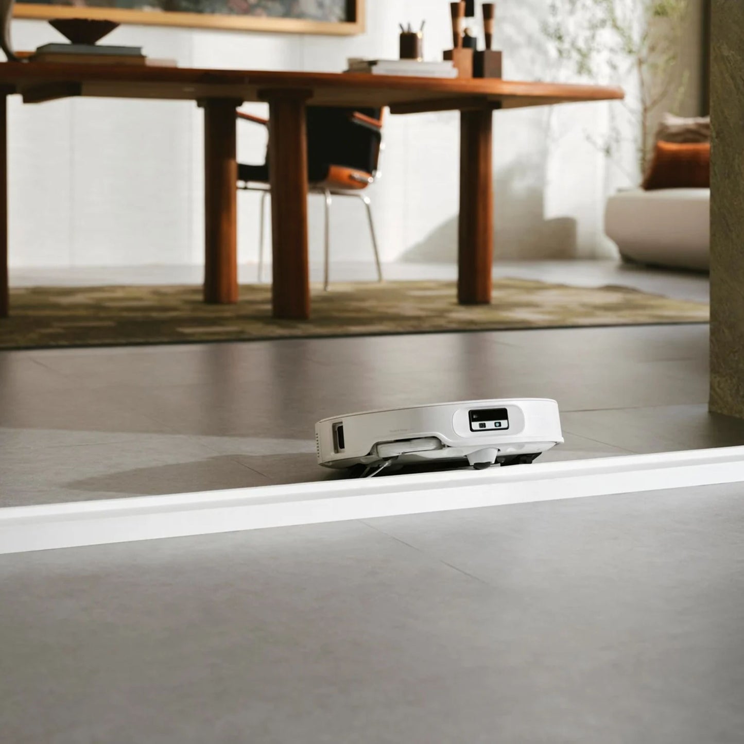 Roborock Qrevo Edge 2 Pro robotstøvsuger med moppe på glat gulv nær træspisebord, stole og tæppe i stue.