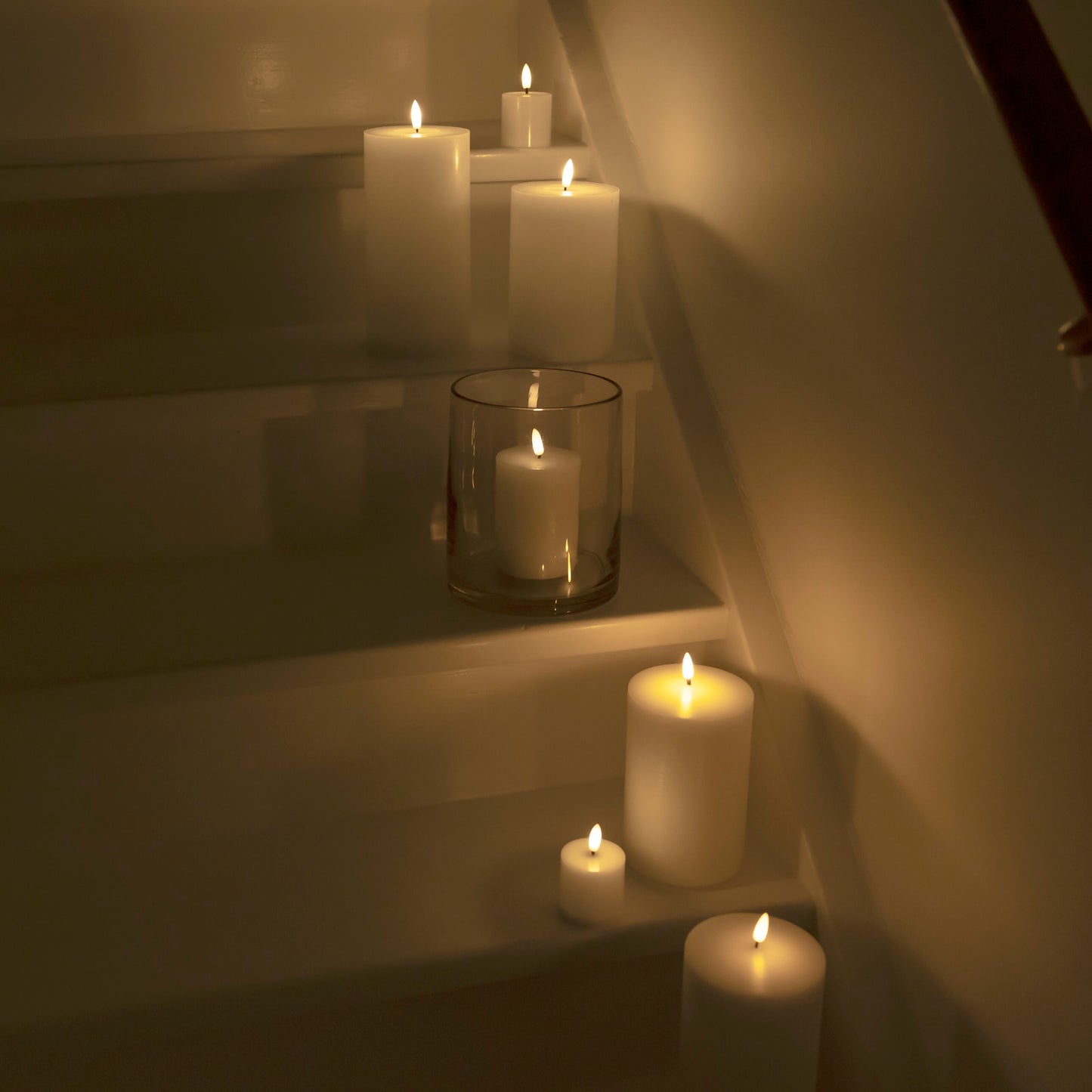 Bloklys LED 3-pakke placeret på hvide trapper langs kanten, lyser med blødt, varmt lys i et dæmpet rum.