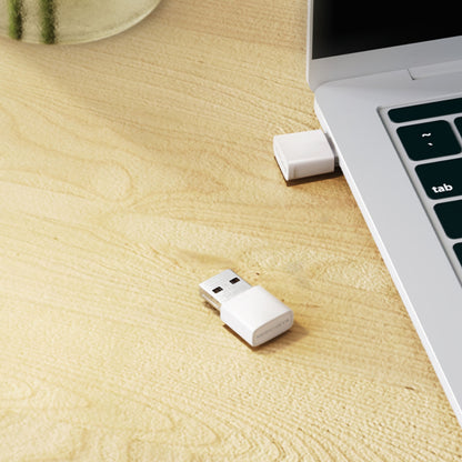 Mercusys MA30N AC1300 USB-netværksadaptere, sort, en tilsluttet og en uden hætte ved siden af sølvlaptop på skrivebord.