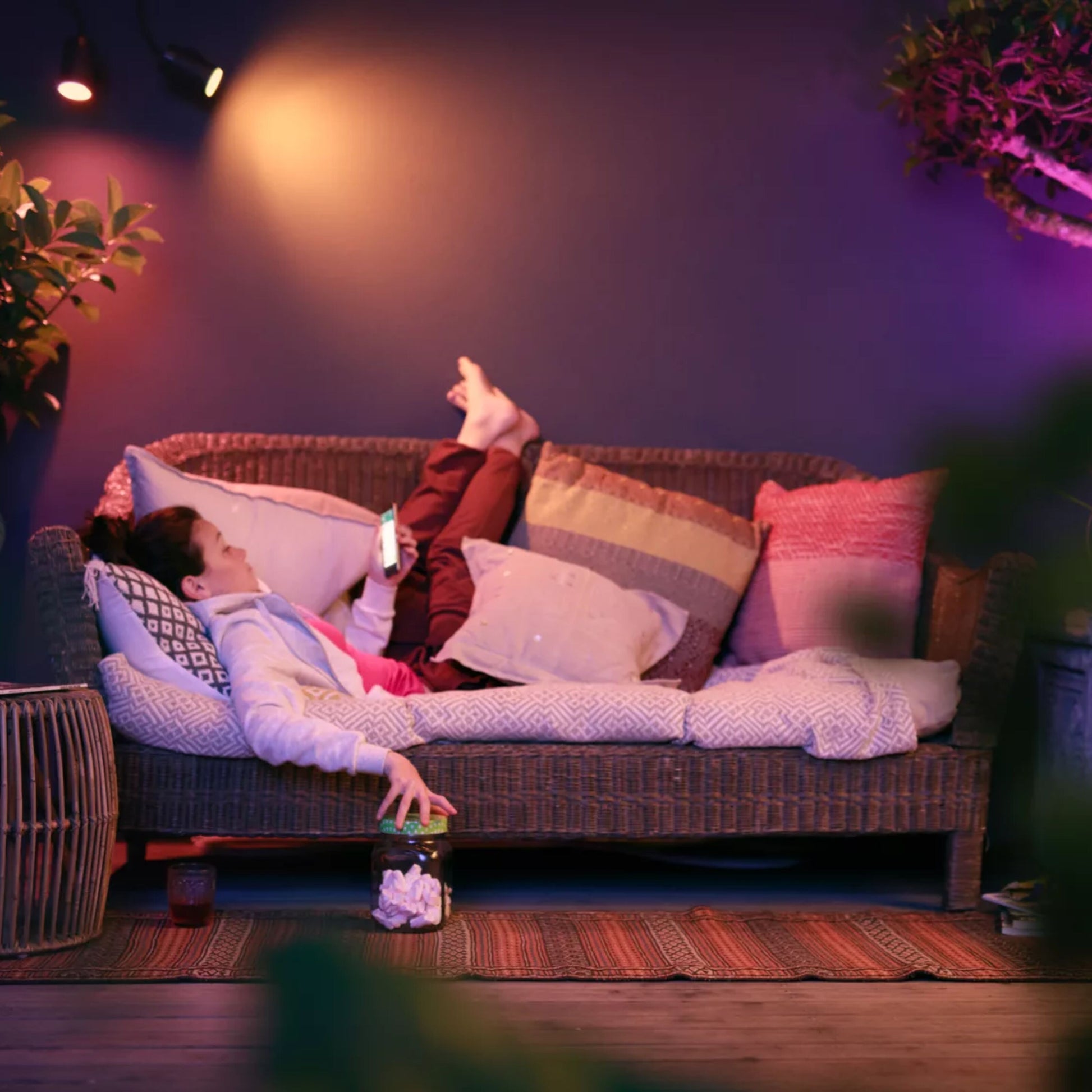 Philips Hue Lily spotlys til udendørs brug 3-pak synlig i blød belysning, omgivet af planter i stueindretning.