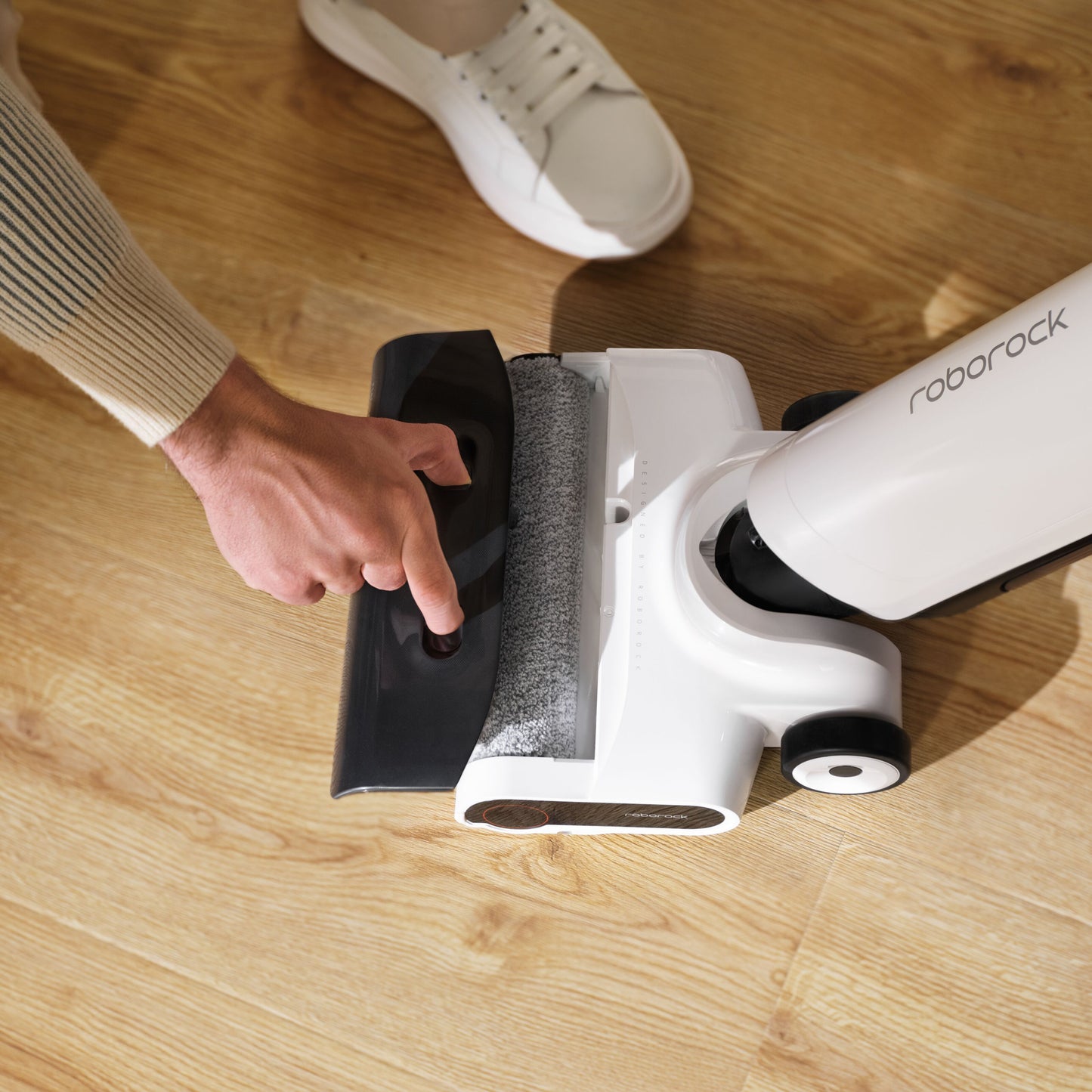 Roborock Flexi Lite stangstøvsuger i hvid, støvbeholder fjernes, trægulv, hvid sko synlig.