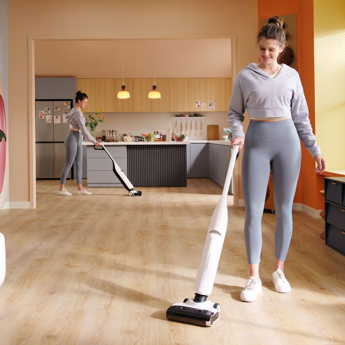 Roborock Flexi Lite stangstøvsuger bruges på trægulv i køkken, kvinde iført lyse leggings, stort spejl reflekterer scenen.