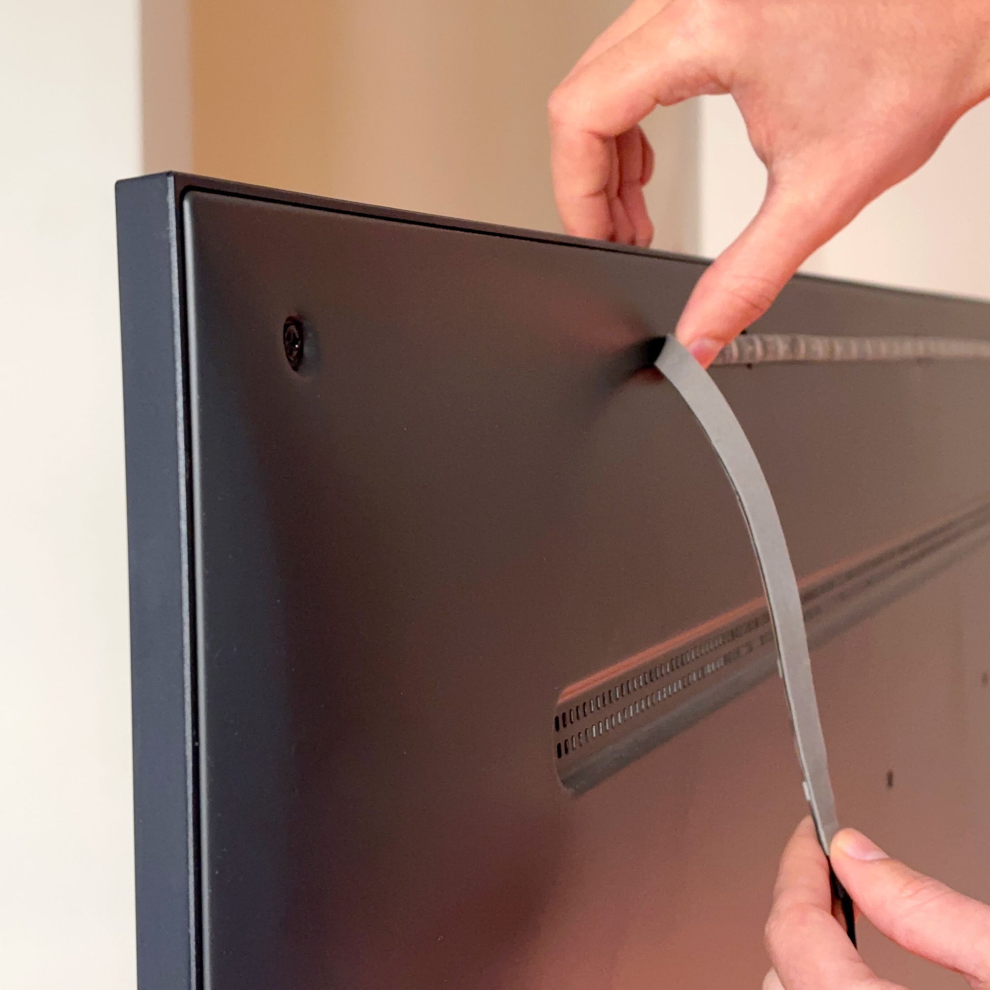 Hænder fjerner tape fra bagsiden af mørkt TV til montering af WiZ Sync box startpakke 55"-65.