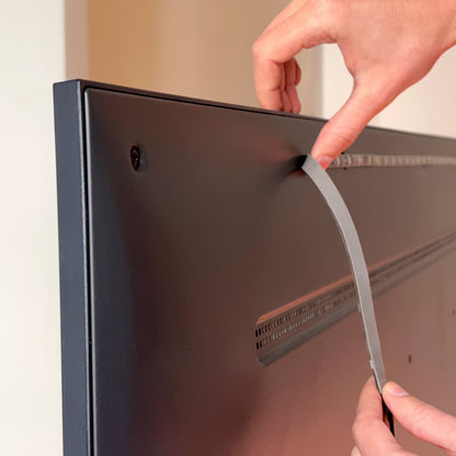 Hænder fjerner tape fra bagsiden af mørkt TV til montering af WiZ Sync box startpakke 55"-65.