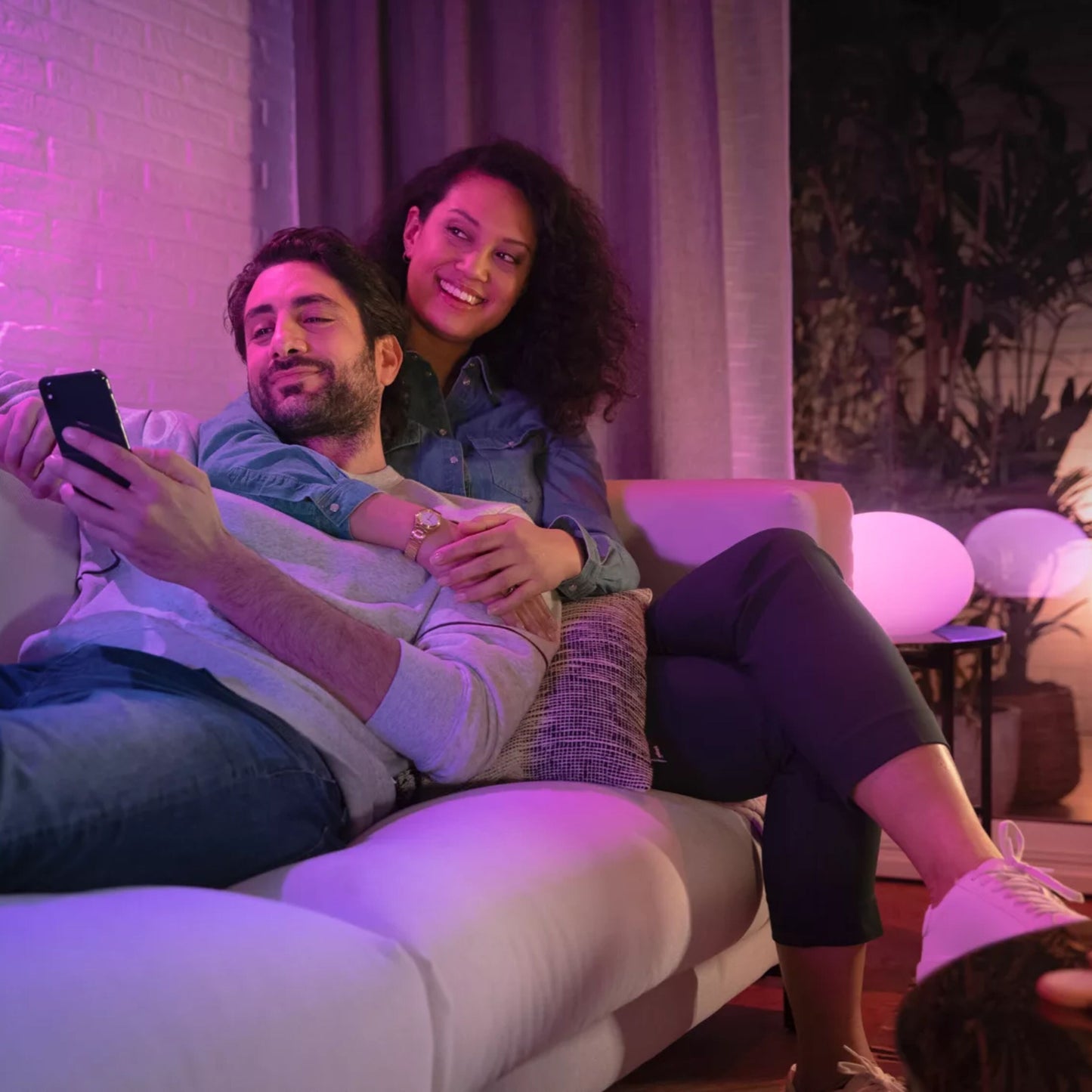 Philips Hue White and Color Ambiance 3x GU10 Smart Startpakke skaber pink og lilla lys i stue med par på sofa.