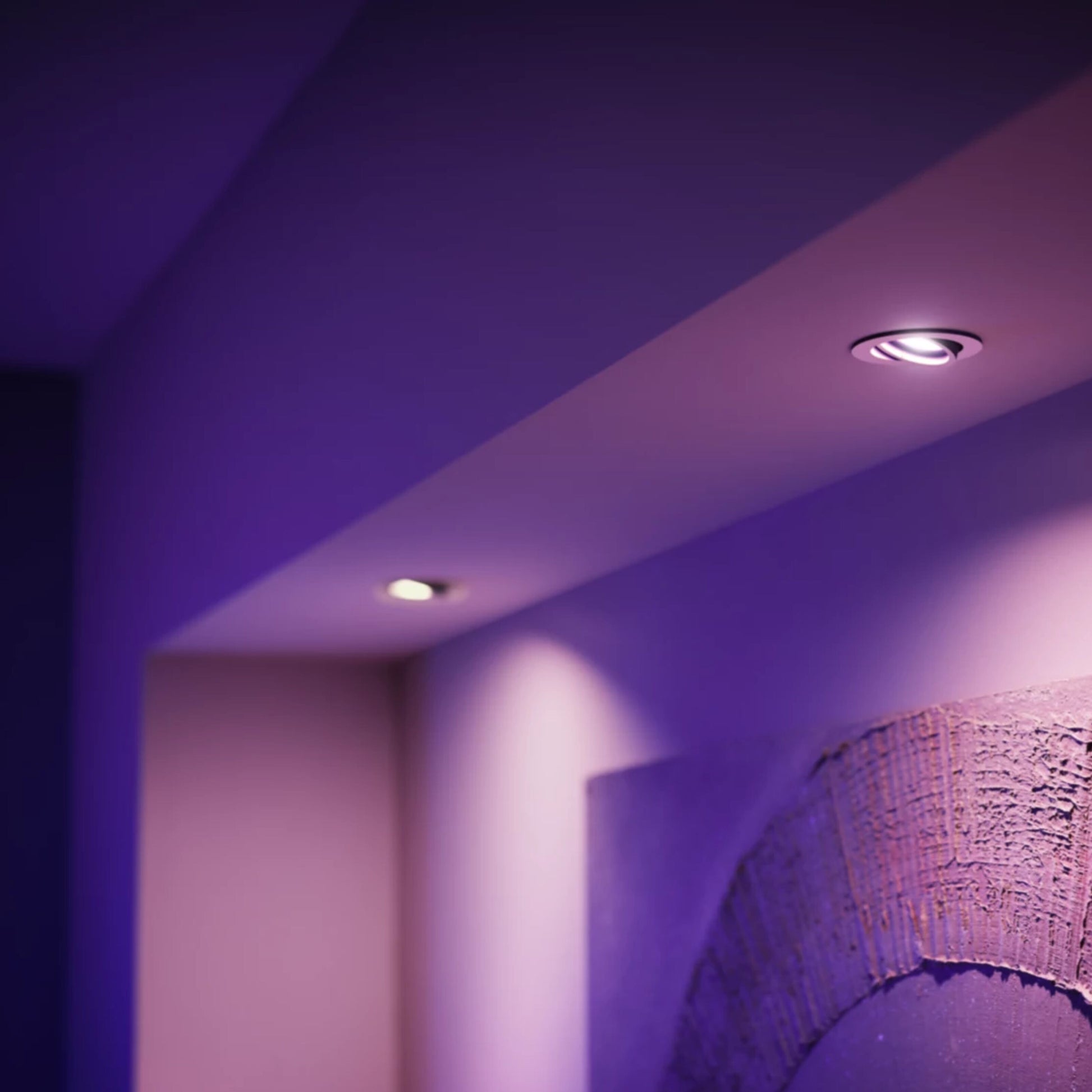 Philips Hue White and Color Ambiance GU10 spotpærer lyser i lilla, tekstureret vægdekoration synlig nederst til højre.