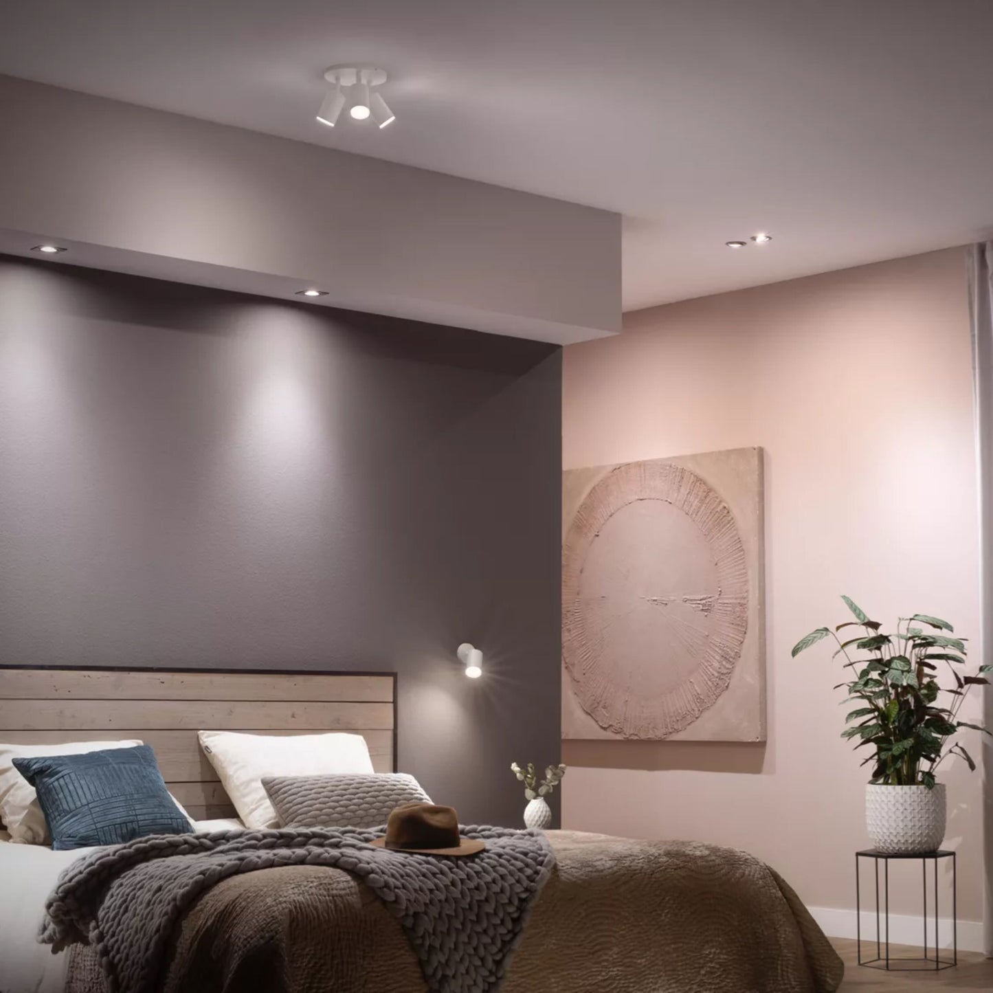 Philips Hue Hvid Ambiance Smart LED-pære GU10 400 lm lyser grå/lyserød væg, træ-seng, hvide/grå dyner, blå/grøn puder.