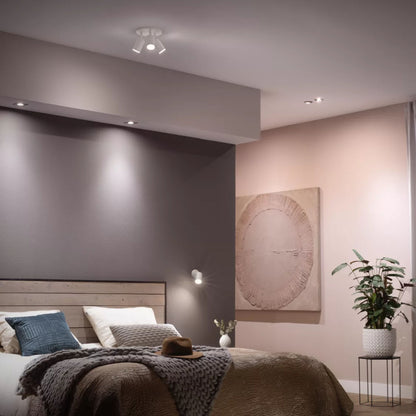 Philips Hue Hvid Ambiance Smart LED-pære GU10 400 lm lyser grå/lyserød væg, træ-seng, hvide/grå dyner, blå/grøn puder.