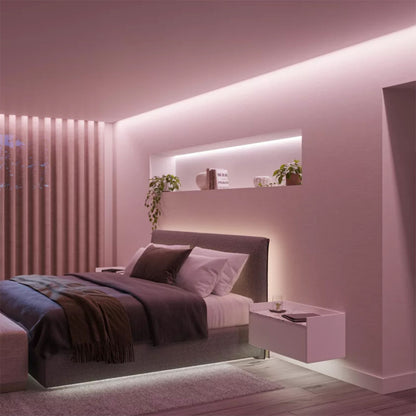 Philips Hue Solo Lightstrip 3 m, pink lys, vises monteret over seng med mørkt sengetøj, træ gulv og svævende natbord.