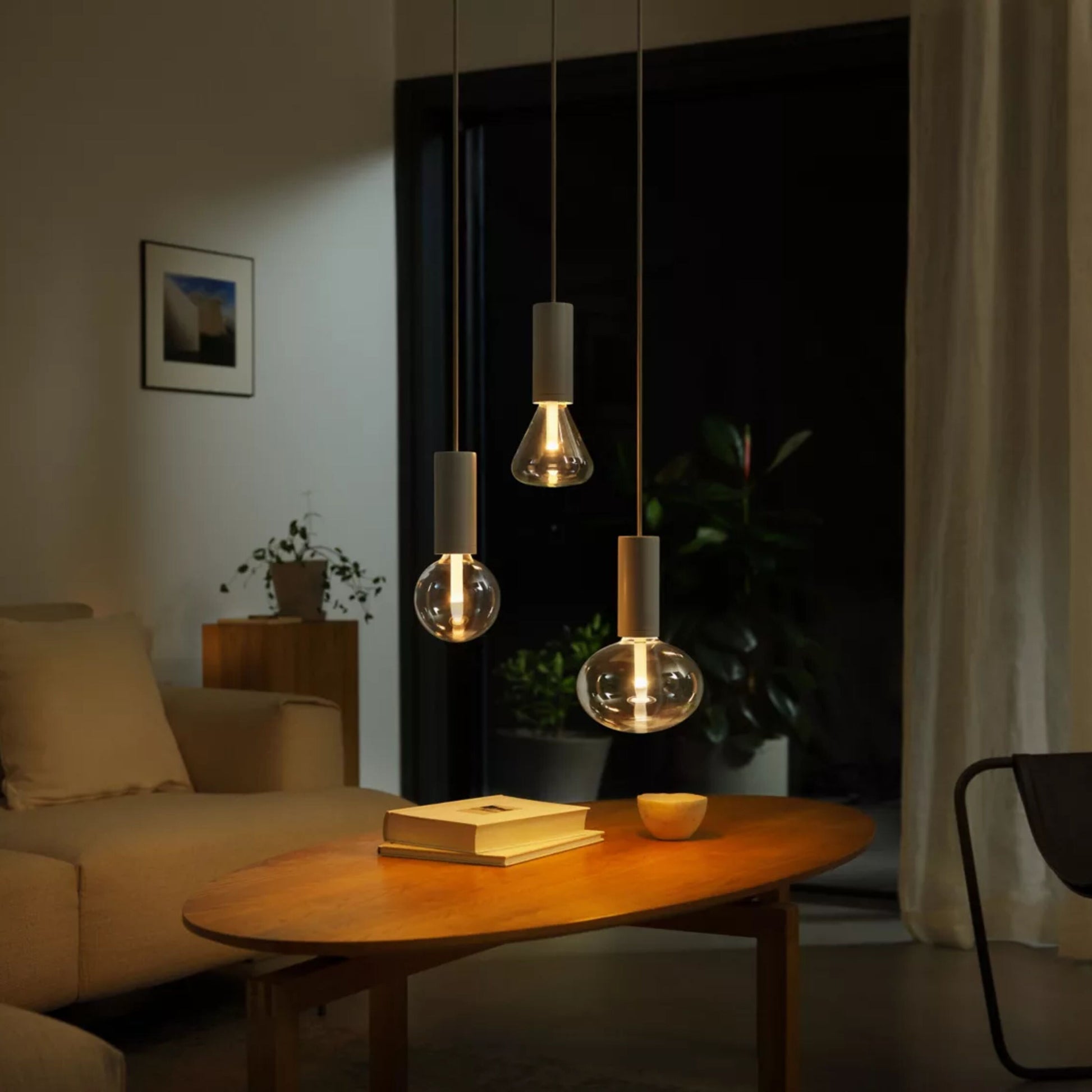 Philips Hue Lightguide G125 E27 smart LED-pære glob 500 lm pendler over sofabord med bøger, beige sofa, grøn plante.