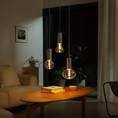 Philips Hue Lightguide G125 E27 smart LED-pære glob 500 lm pendler over sofabord med bøger, beige sofa, grøn plante.