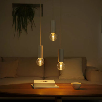 Philips Hue RGB G95 Smart LED-pære E27 500 lm over sofabord med bog og kop, beige sofa og plante ses i baggrunden.