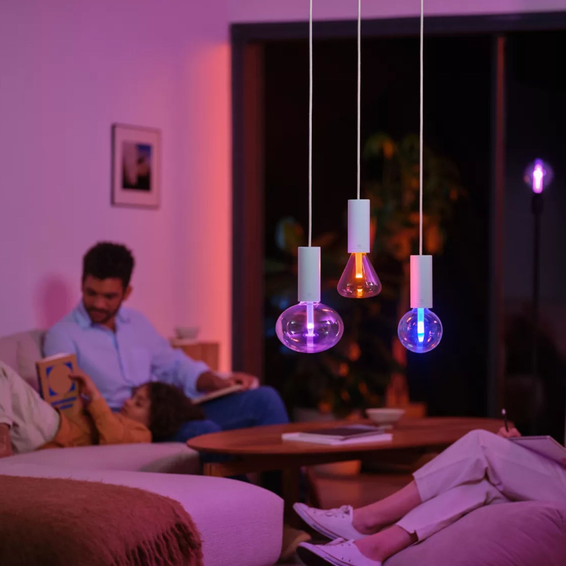 Philips Hue RGB G95 Smart LED-pære E27 500 lm, tre pendellamper, varm og lilla belysning over sofaområde.