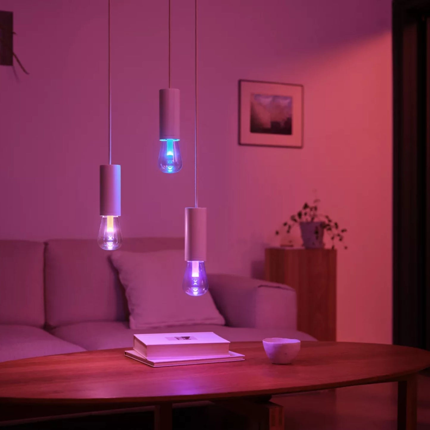 Philips Hue RGB ST72 smart LED-pære E27 500 lm i tre pendler over sofabord, lilla-lyserød belysning i stuen.