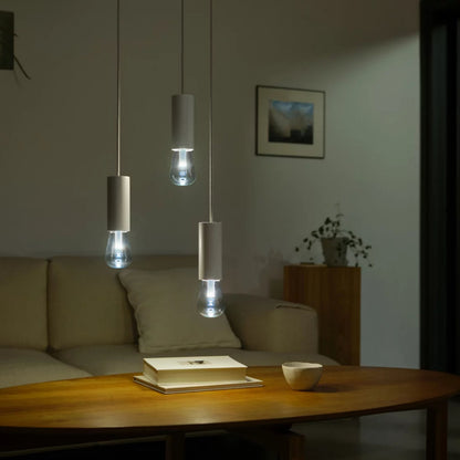 RGB ST72 smart LED-pære E27 500 lm monteret i tre pendler over trækakkebord med bøger og kop, beige sofa i baggrunden.