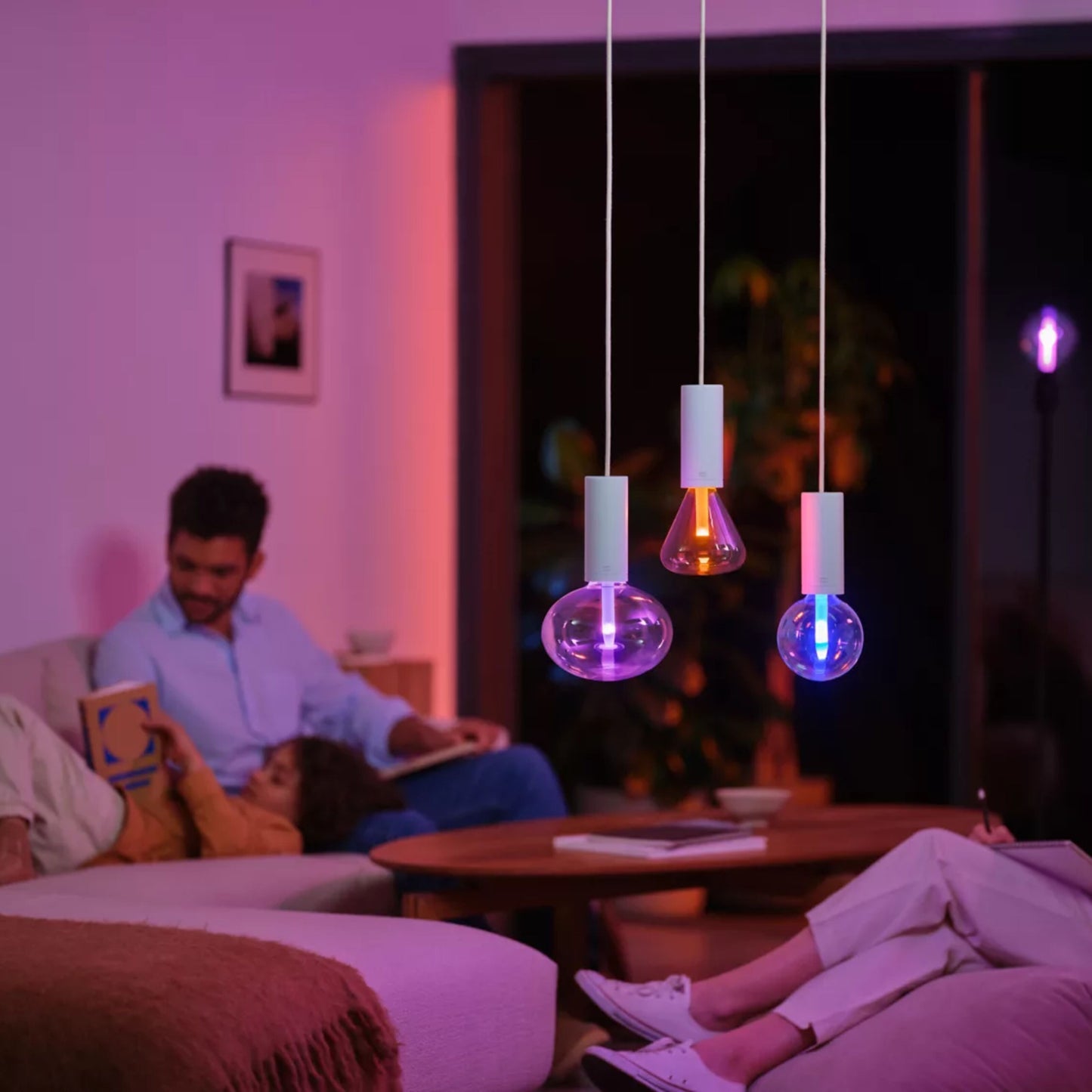 Philips Hue Lightguide Triangle E27 smart LED-pærer 500 lm som pendellamper over sofabord, folk sidder i stue.