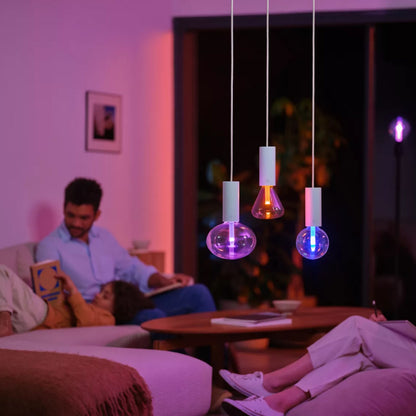 Philips Hue Lightguide Triangle E27 smart LED-pærer 500 lm som pendellamper over sofabord, folk sidder i stue.