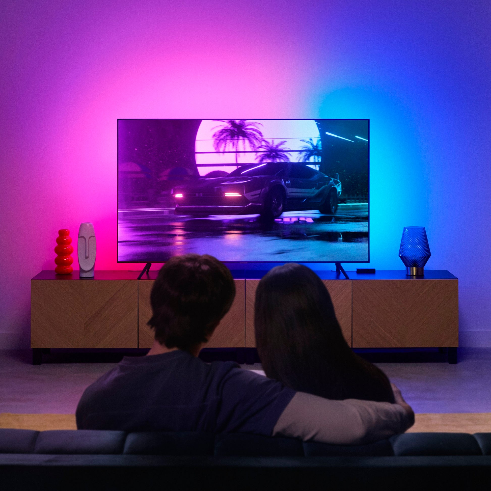 WiZ Sync box startpakke 75"-85" RGBIC lyser op bag stor TV-skærm placeret på træ-tv-bord i moderne stue.