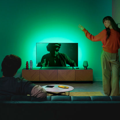 WiZ Sync box startpakke 75"-85" med RGBIC giver grøn belysning omkring TV i moderne stue, mand ser TV.